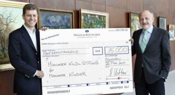 Robert Ketterer, Auktionator und Inhaber von Ketterer Kunst (links) übergibt Christian Netzer, Vorstandsvorsitzender der Münchner Kindl-Stiftung (rechts) einen Scheck mit der bei der Versteigerung erlösten Summe von € 15.000