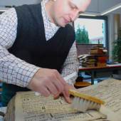 Mit einer Bürste reinigt Gerit Depping die Seiten eines fast 500 Jahre alten Buchs mit Messgesängen. Sein Handwerk zeigt er auch auf den Kunst- und Antiquitäten-Tagen.